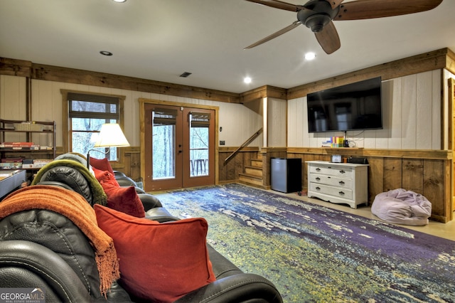 living room featuring ceiling fan, light colored carpet, wooden walls, and french doors