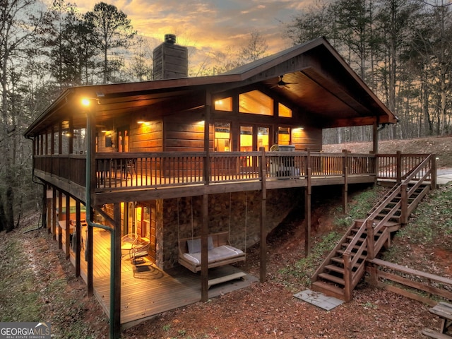 back house at dusk featuring a sunroom, ceiling fan, and a wooden deck