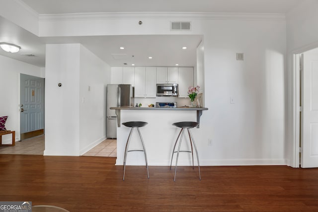 kitchen with appliances with stainless steel finishes, kitchen peninsula, white cabinetry, light hardwood / wood-style floors, and a breakfast bar