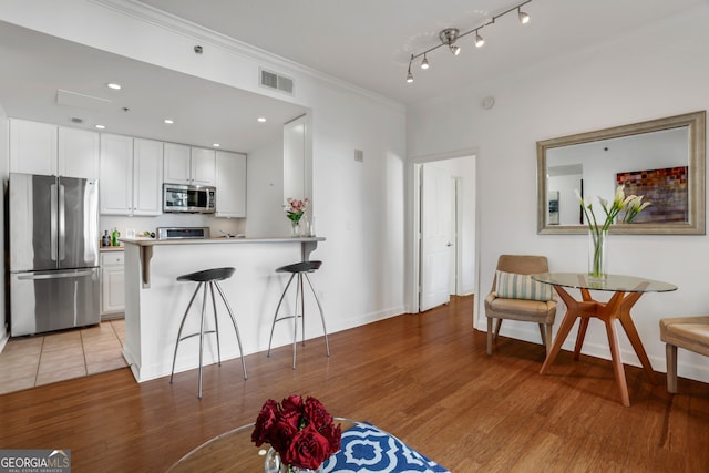 kitchen with a kitchen bar, kitchen peninsula, light hardwood / wood-style floors, stainless steel appliances, and white cabinets