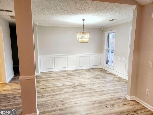 unfurnished dining area featuring a textured ceiling, a chandelier, light wood-type flooring, and decorative columns