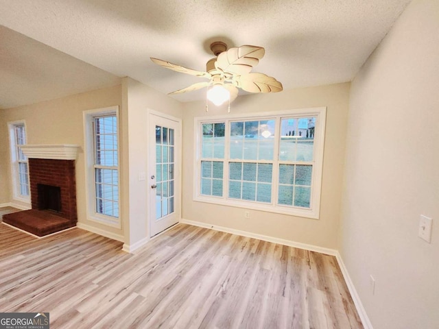 unfurnished living room with light hardwood / wood-style flooring, a textured ceiling, ceiling fan, and a brick fireplace