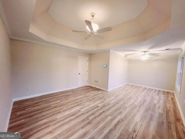 empty room featuring ceiling fan, light wood-type flooring, and a raised ceiling