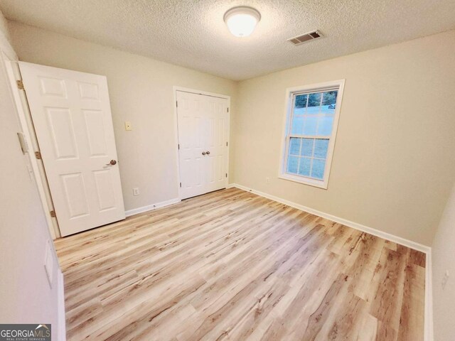 unfurnished bedroom with a closet, a textured ceiling, and light wood-type flooring