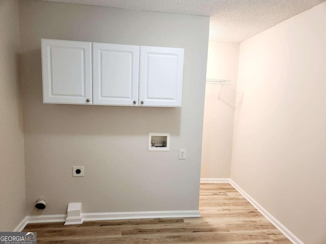 clothes washing area featuring hookup for an electric dryer, a textured ceiling, light hardwood / wood-style floors, washer hookup, and cabinets