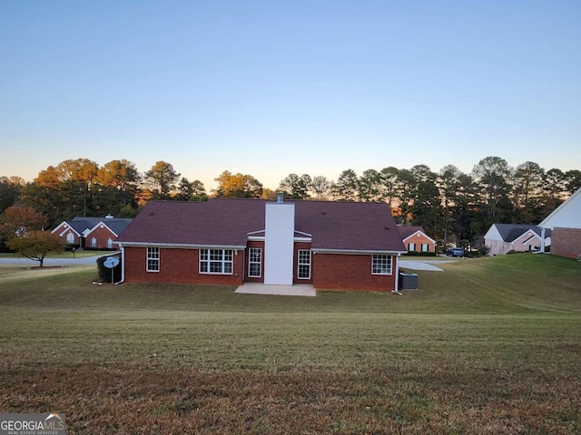 back house at dusk with a patio and a lawn