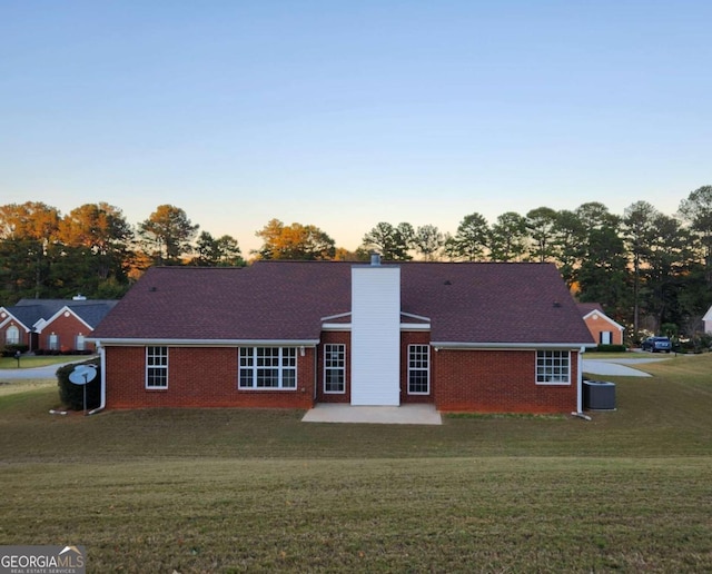 back house at dusk featuring a patio area and a lawn