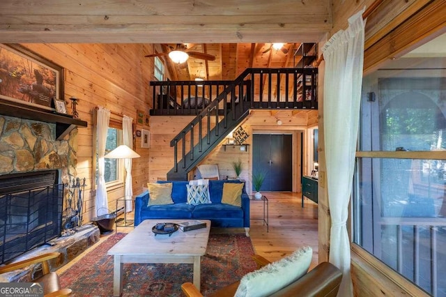 living room featuring beam ceiling, ceiling fan, a stone fireplace, wooden walls, and hardwood / wood-style flooring