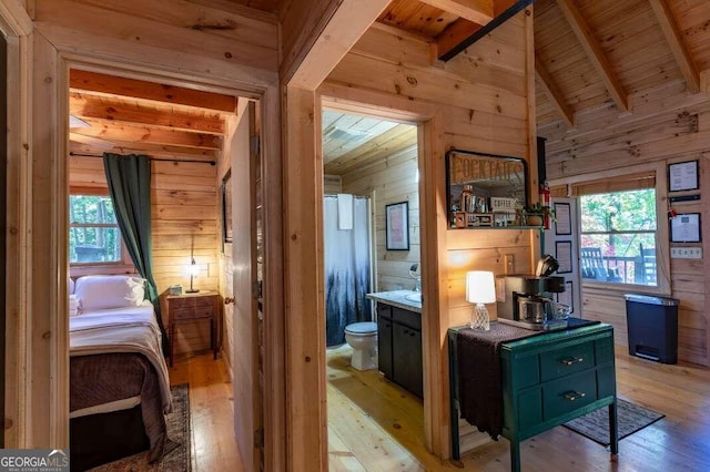 interior space with light wood finished floors, vaulted ceiling with beams, wood walls, wood ceiling, and ensuite bathroom