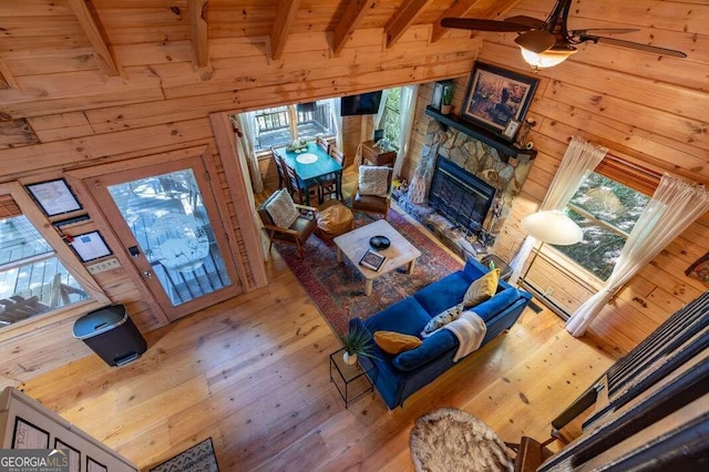 living room with hardwood / wood-style floors, beam ceiling, ceiling fan, and wood walls