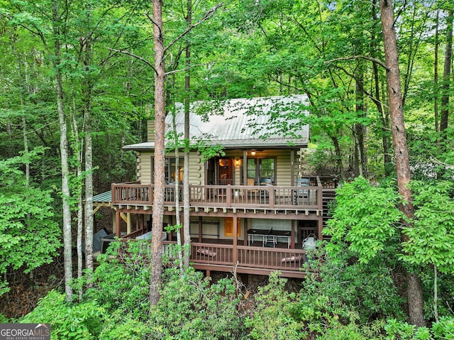 rear view of property with a forest view, a deck, and metal roof