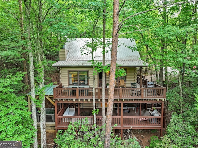 back of property featuring a wooden deck, a wooded view, log exterior, and metal roof