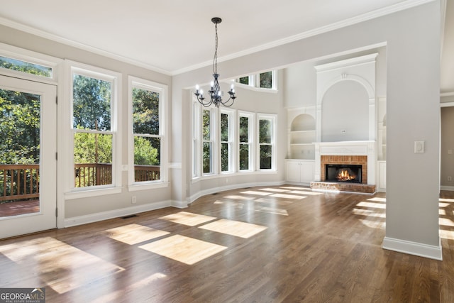 unfurnished living room featuring built in features, a brick fireplace, dark wood-type flooring, ornamental molding, and a chandelier