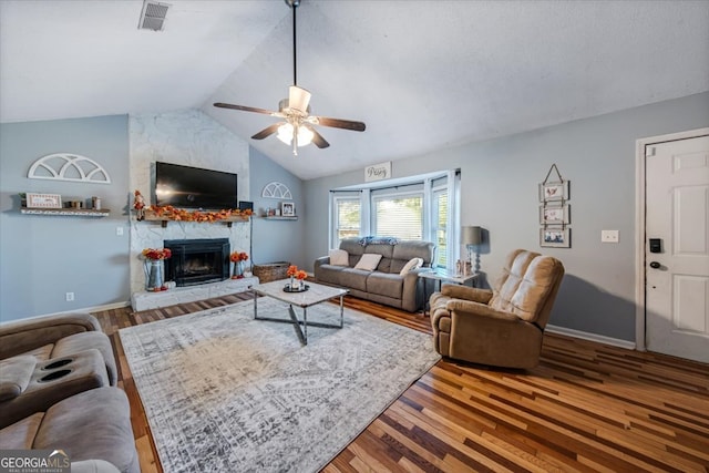 living room with a stone fireplace, ceiling fan, wood-type flooring, and vaulted ceiling