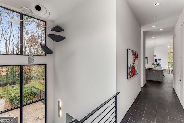 hall featuring a healthy amount of sunlight, dark tile patterned floors, and a high ceiling