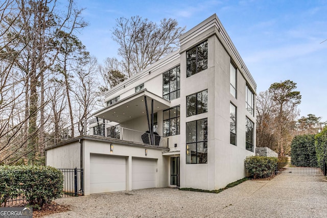 view of front of home with gravel driveway, fence, a balcony, and stucco siding