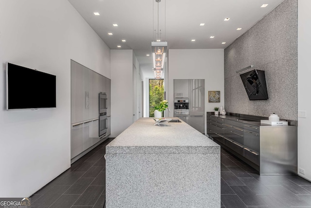 kitchen with modern cabinets, an accent wall, a kitchen island with sink, light countertops, and recessed lighting