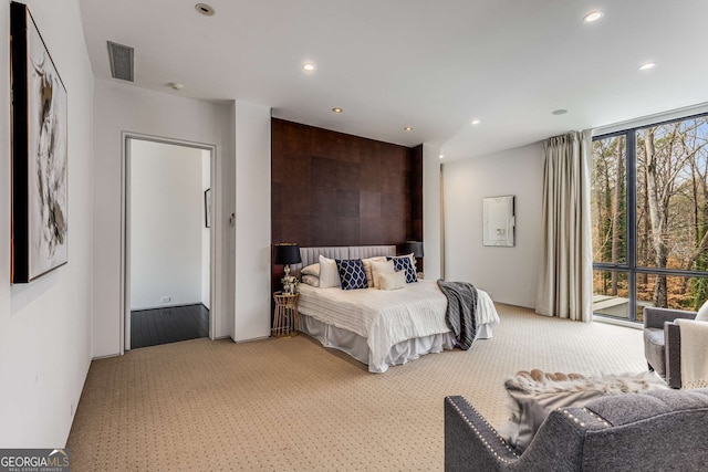 carpeted bedroom with an accent wall, expansive windows, visible vents, and recessed lighting