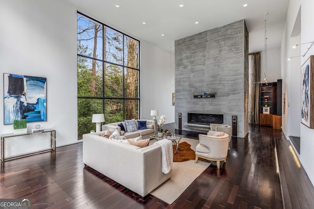 living area with a high ceiling, a fireplace, wood finished floors, a healthy amount of sunlight, and floor to ceiling windows