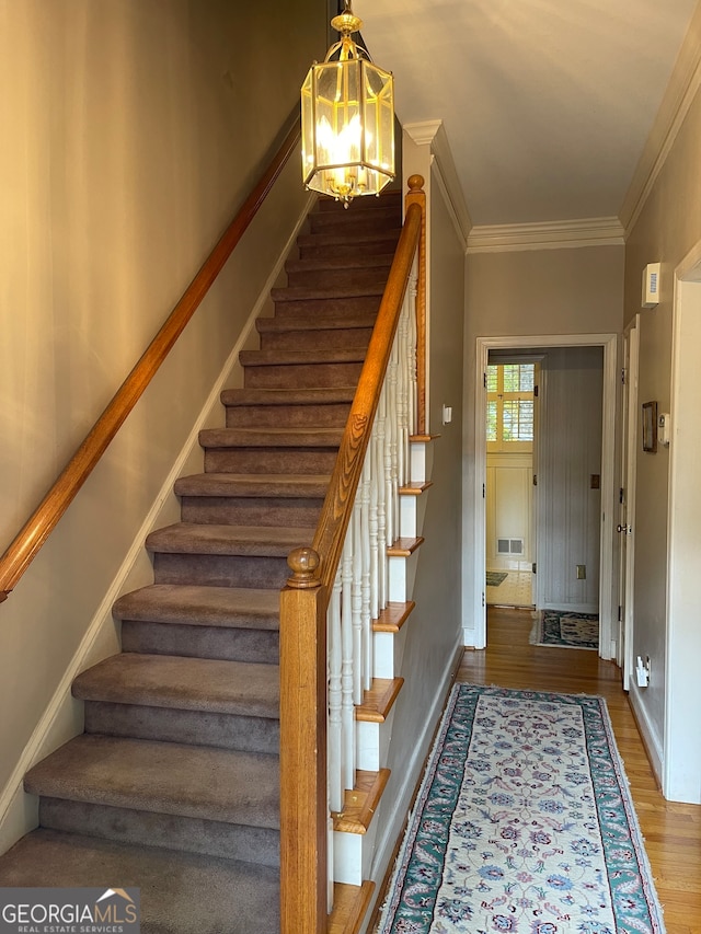 stairway with ornamental molding, hardwood / wood-style floors, and a notable chandelier