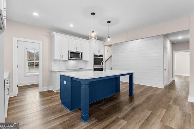 kitchen featuring a kitchen island with sink, hanging light fixtures, decorative backsplash, white cabinetry, and stainless steel appliances