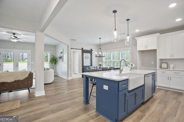 kitchen with sink, a barn door, an island with sink, decorative light fixtures, and white cabinetry