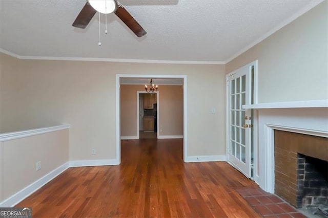 empty room featuring dark hardwood / wood-style floors, crown molding, a brick fireplace, a textured ceiling, and ceiling fan with notable chandelier