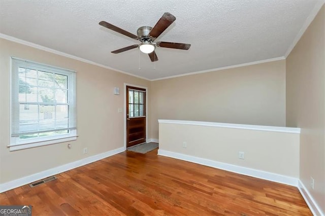 empty room with ornamental molding, a textured ceiling, a wealth of natural light, and hardwood / wood-style floors