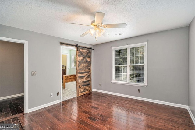 unfurnished bedroom with a textured ceiling, a barn door, dark wood-type flooring, and ceiling fan