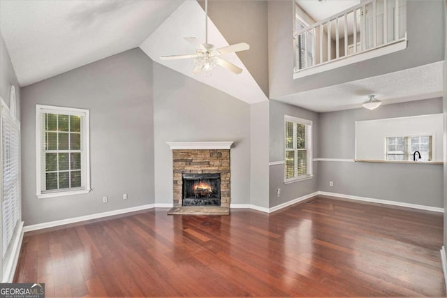 unfurnished living room with a stone fireplace, a textured ceiling, ceiling fan, high vaulted ceiling, and dark hardwood / wood-style floors