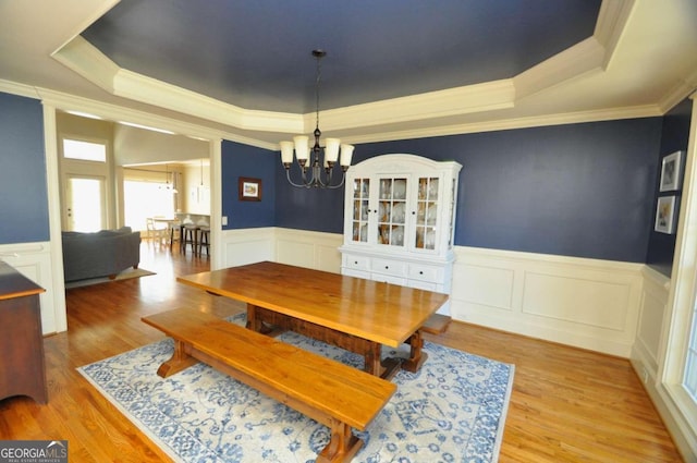 dining room with light hardwood / wood-style floors, crown molding, a notable chandelier, and a raised ceiling