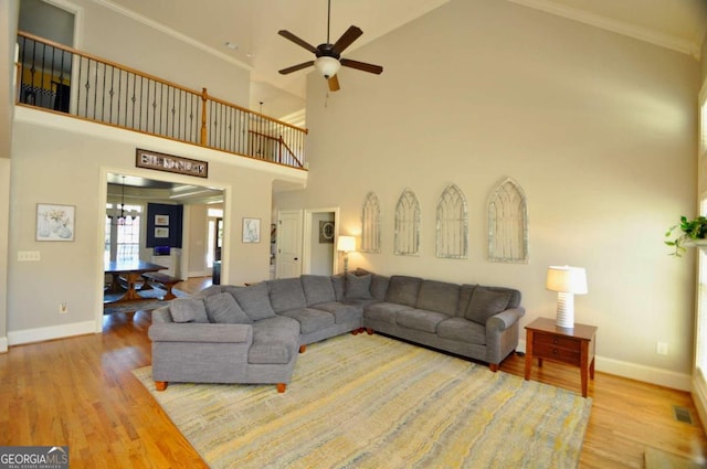 living room with ornamental molding, ceiling fan with notable chandelier, hardwood / wood-style flooring, and high vaulted ceiling