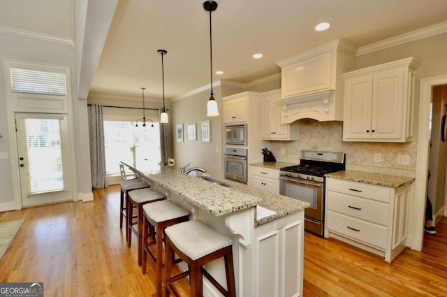 kitchen featuring a kitchen island with sink, stainless steel appliances, light wood-type flooring, and white cabinetry