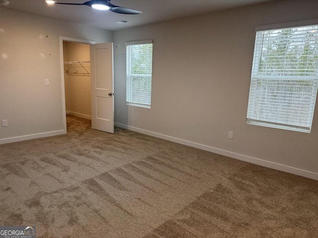 unfurnished bedroom with a spacious closet, multiple windows, a closet, carpet flooring, and ceiling fan