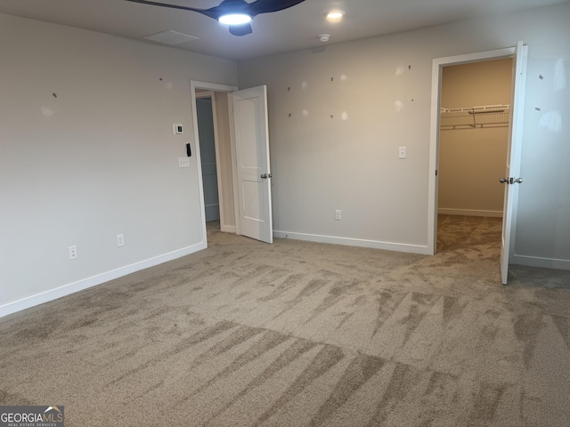 unfurnished bedroom featuring ceiling fan, a walk in closet, a closet, and light colored carpet