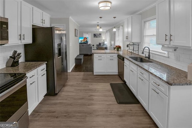 kitchen featuring kitchen peninsula, light wood-type flooring, stainless steel appliances, pendant lighting, and white cabinetry