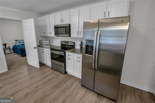 kitchen with decorative backsplash, dark stone counters, stainless steel appliances, white cabinets, and light hardwood / wood-style floors