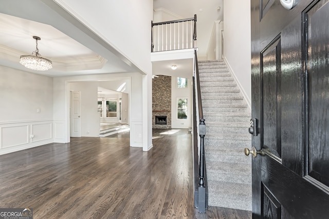 entryway featuring a raised ceiling, dark hardwood / wood-style flooring, an inviting chandelier, ornamental molding, and a fireplace