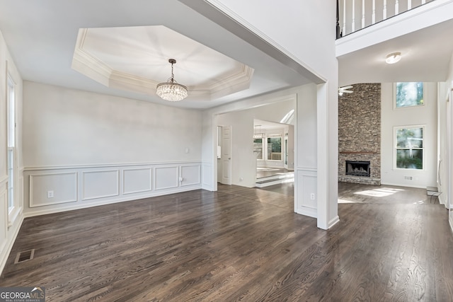 unfurnished living room featuring a raised ceiling, ornamental molding, dark hardwood / wood-style flooring, and a fireplace