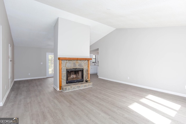 unfurnished living room with a fireplace, light wood-type flooring, and vaulted ceiling