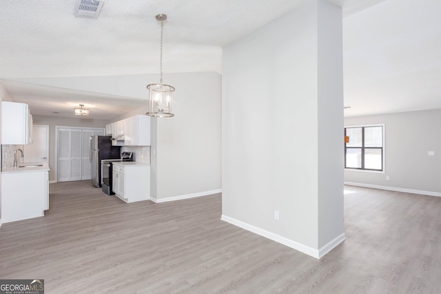 unfurnished living room featuring light wood-type flooring, a textured ceiling, vaulted ceiling, sink, and a notable chandelier