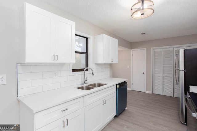 kitchen featuring sink, stainless steel appliances, a textured ceiling, white cabinets, and light wood-type flooring