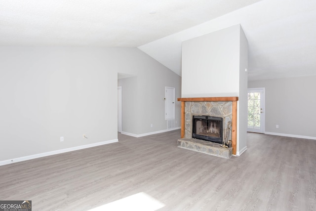 unfurnished living room with a stone fireplace, vaulted ceiling, and light wood-type flooring