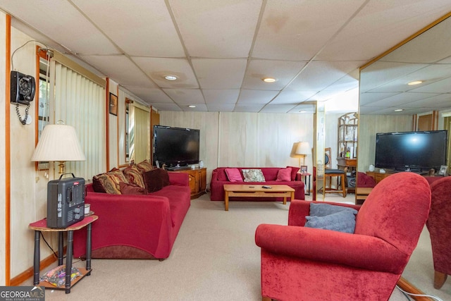 living room featuring carpet flooring, a drop ceiling, and wood walls