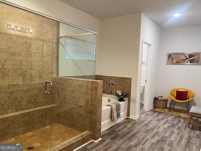 bathroom featuring toilet, wood-type flooring, and shower with separate bathtub