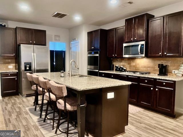 kitchen with sink, an island with sink, a kitchen bar, appliances with stainless steel finishes, and light wood-type flooring