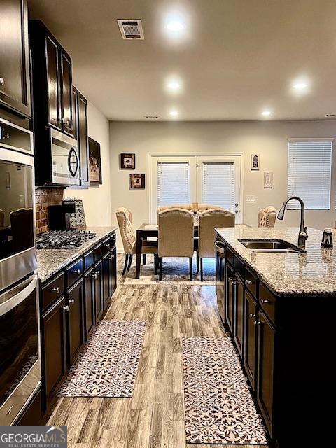 kitchen with light stone countertops, dark brown cabinets, stainless steel appliances, sink, and light hardwood / wood-style floors