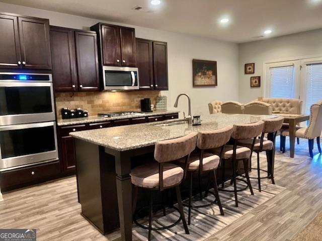 kitchen with appliances with stainless steel finishes, an island with sink, light hardwood / wood-style floors, and sink