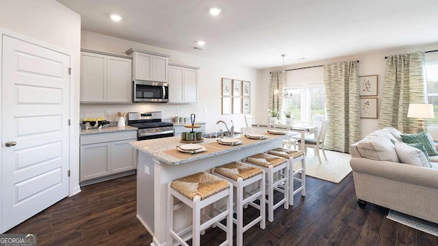 kitchen with dark hardwood / wood-style floors, a kitchen island with sink, stainless steel appliances, and hanging light fixtures