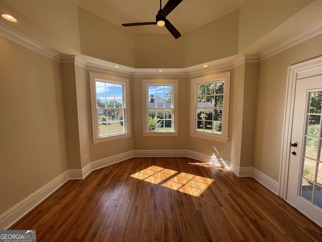 unfurnished room with a towering ceiling, crown molding, dark wood-type flooring, and ceiling fan